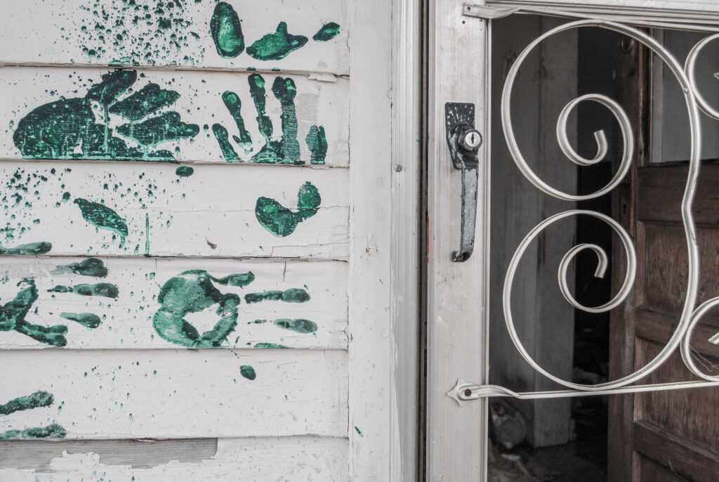 Green handprints on siding beside a wrought iron door, Chat Heap photography by Chuck Davis